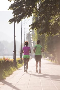 healthy young multiethnic couple jogging in the city at early morning with sunrise in background