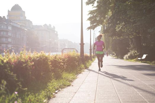 Beautiful young sporty african american woman running at early morning jogging with city sunrise scene in background