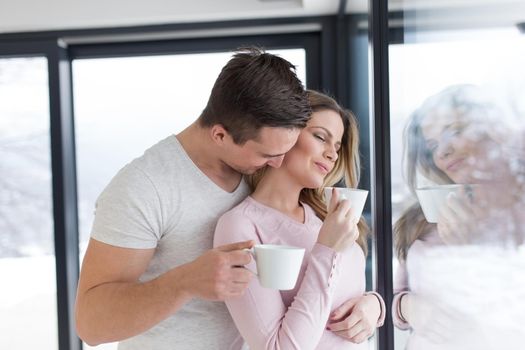 romantic happy young couple enjoying morning coffee by the window on cold winter day at home