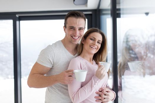 romantic happy young couple enjoying morning coffee by the window on cold winter day at home