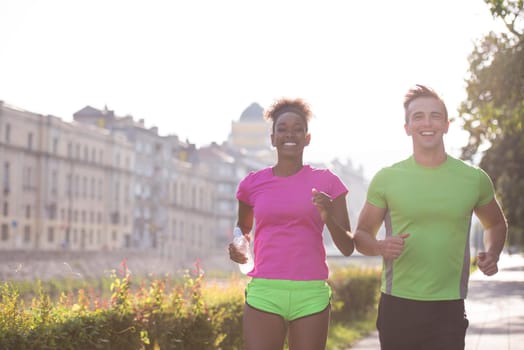 healthy young multiethnic couple jogging in the city at early morning with sunrise in background