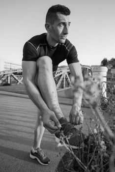 man tying running shoes laces getting ready to run on city at sunny morning