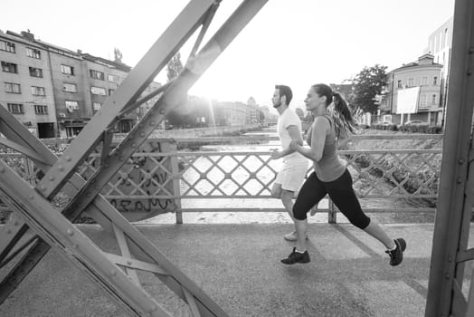 urban sports, healthy young couple jogging across the bridge in the city at sunny morning