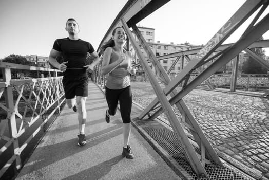 urban sports, healthy young couple jogging across the bridge in the city at sunny morning