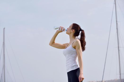 Young beautiful woman drinking water after fitness exercise and jogging outdoors