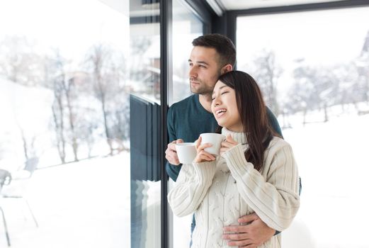 happy young multiethnic couple enjoying morning coffee by the window on cold winter day at home