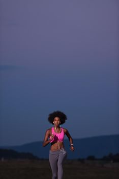 young African american woman runner with headphones jogging outdoors in nature beautiful summer night - Fitness, people and healthy lifestyle