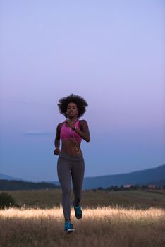 young African american woman runner with headphones jogging outdoors in nature beautiful summer night - Fitness, people and healthy lifestyle