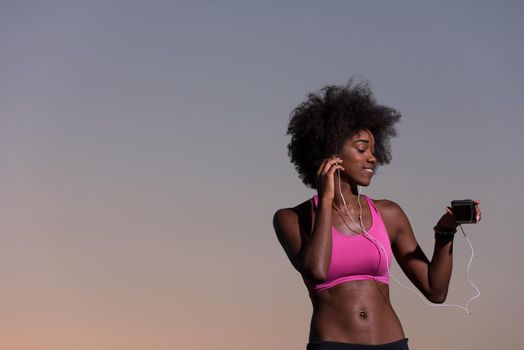 portrait of a young beautiful african american woman with headphones and mobile phone jogging in nature beautiful summer night