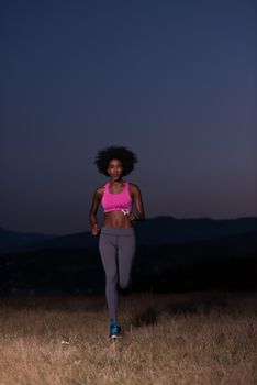 young African american woman runner with headphones jogging outdoors in nature beautiful summer night - Fitness, people and healthy lifestyle