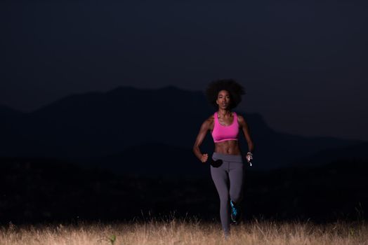 young African american woman runner with headphones jogging outdoors in nature beautiful summer night - Fitness, people and healthy lifestyle