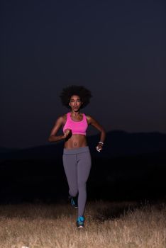 young African american woman runner with headphones jogging outdoors in nature beautiful summer night - Fitness, people and healthy lifestyle