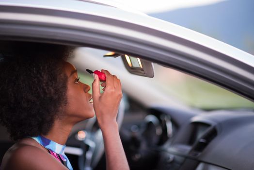 young beautiful African American woman enjoys while makeup herself in the car