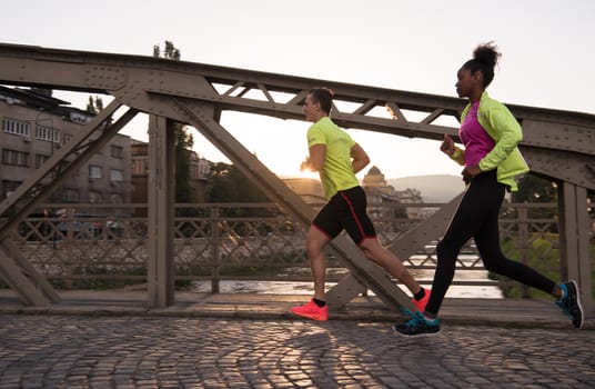 healthy young multiethnic couple jogging in the city at early morning with sunrise in background