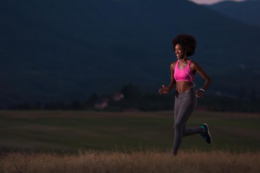 young African american woman runner with headphones jogging outdoors in nature beautiful summer night - Fitness, people and healthy lifestyle