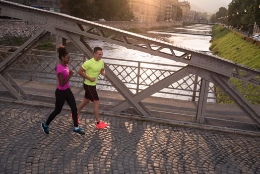 healthy young multiethnic couple jogging in the city at early morning with sunrise in background