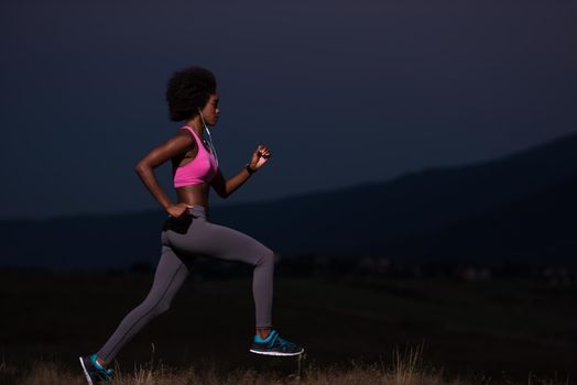 young African american woman runner with headphones jogging outdoors in nature beautiful summer night - Fitness, people and healthy lifestyle