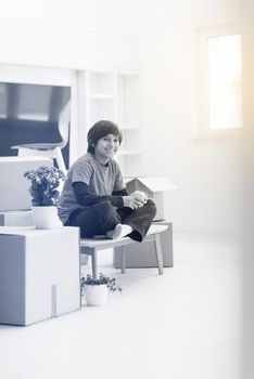 happy little boy sitting on the table with cardboard boxes around him in a new modern home