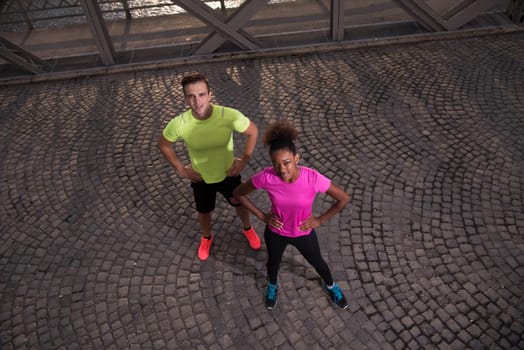 portrait of a healthy young multiethnic couple jogging in the city at early morning with sunrise in background