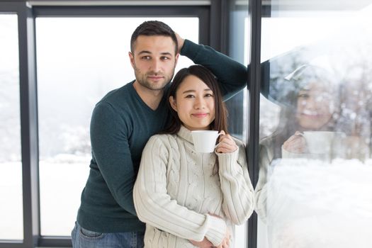 happy young multiethnic couple enjoying morning coffee by the window on cold winter day at home