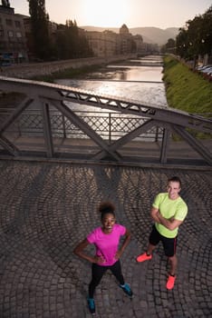 portrait of a healthy young multiethnic couple jogging in the city at early morning with sunrise in background
