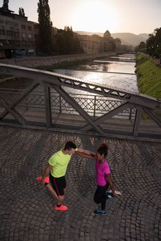 Young multiethnic jogging couple warming up and stretching before morning running in the city