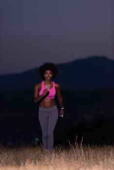 young African american woman runner with headphones jogging outdoors in nature beautiful summer night - Fitness, people and healthy lifestyle