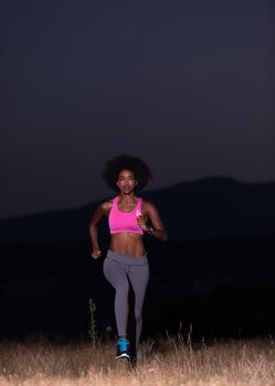 young African american woman runner with headphones jogging outdoors in nature beautiful summer night - Fitness, people and healthy lifestyle