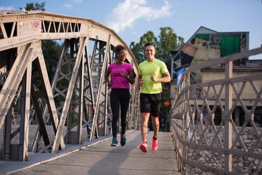 healthy young multiethnic couple jogging across the bridge in the city at early morning with sunrise in background