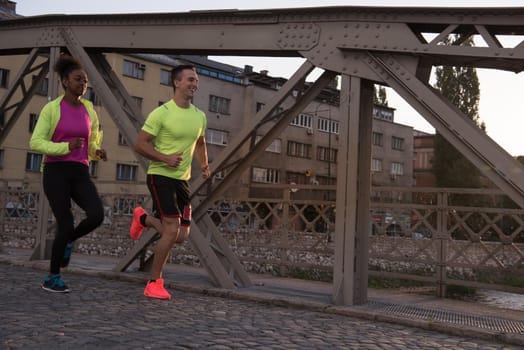 healthy young multiethnic couple jogging in the city at early morning with sunrise in background