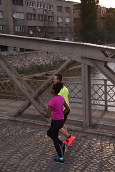 healthy young multiethnic couple jogging in the city at early morning with sunrise in background