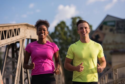 healthy young multiethnic couple jogging across the bridge in the city at early morning with sunrise in background