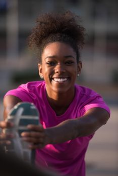 young beautiful African American woman doing warming up and stretching with her leg raised to the bridge before the morning run with the sunrise in the background