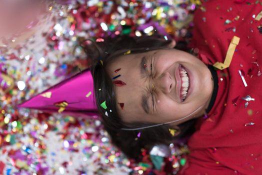 Happy kid celebrating party with blowing confetti while lying on the floor