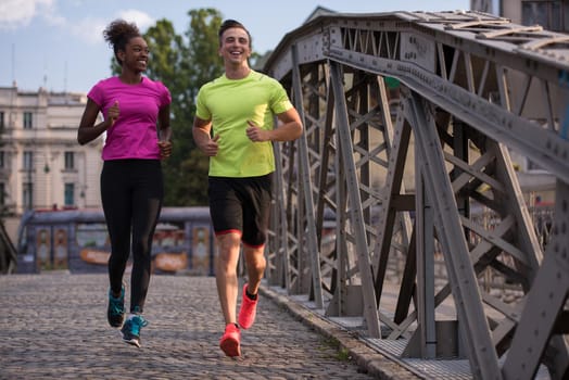 healthy young multiethnic couple jogging across the bridge in the city at early morning with sunrise in background