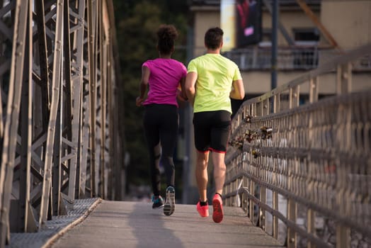 healthy young multiethnic couple jogging across the bridge in the city at early morning with sunrise in background