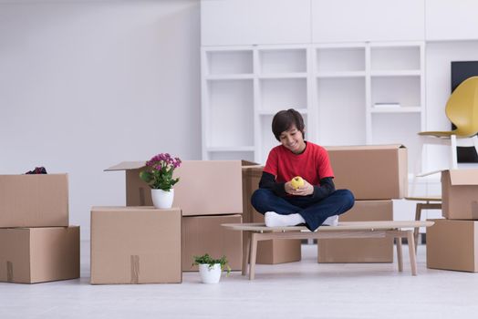 happy little boy sitting on the table with cardboard boxes around him in a new modern home