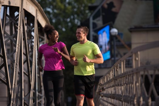 healthy young multiethnic couple jogging across the bridge in the city at early morning with sunrise in background