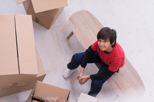 happy little boy sitting on the table with cardboard boxes around him in a new modern home,top view