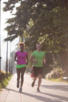 healthy young multiethnic couple jogging in the city at early morning with sunrise in background