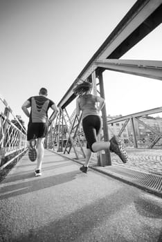 urban sports, healthy young couple jogging across the bridge in the city at sunny morning