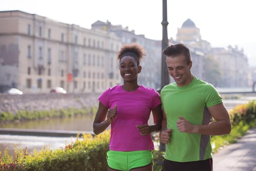 healthy young multiethnic couple jogging in the city at early morning with sunrise in background