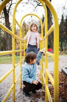 cutte little girl and boy in childrens park having fun and joy while playing in playground on autumn cloudy day