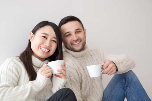 happy young multiethnic couple enjoying morning coffee by the window on cold winter day at home