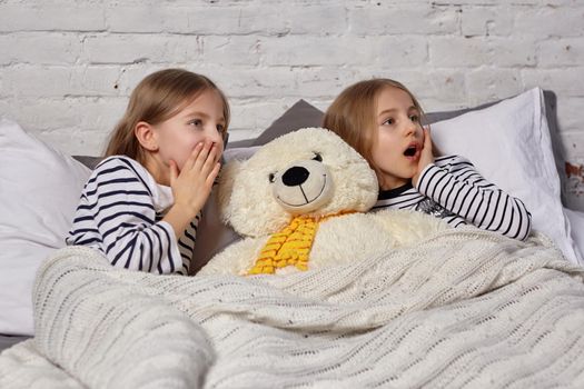 The image of two little sisters waking up in the morning. Big white plush toy bear laying between them. Something scared them