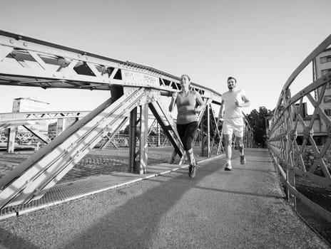 urban sports, healthy young couple jogging across the bridge in the city at sunny morning