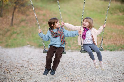 cheerful children are having fun on a swing little brother and sister playing outside