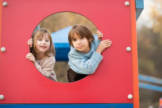 cutte little girl and boy in childrens park having fun and joy while playing in playground on autumn cloudy day