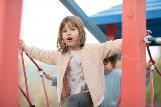 cutte little girl and boy in childrens park having fun and joy while playing in playground on autumn cloudy day