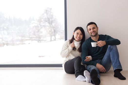 happy young multiethnic couple enjoying morning coffee by the window on cold winter day at home